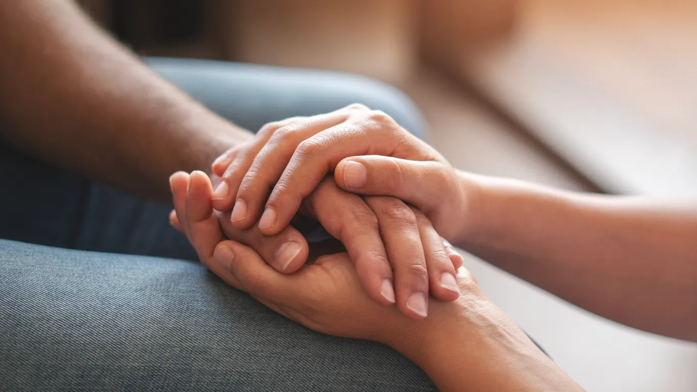 Two people gently holding hands in a close-up moment of comfort and compassion during grief therapy.