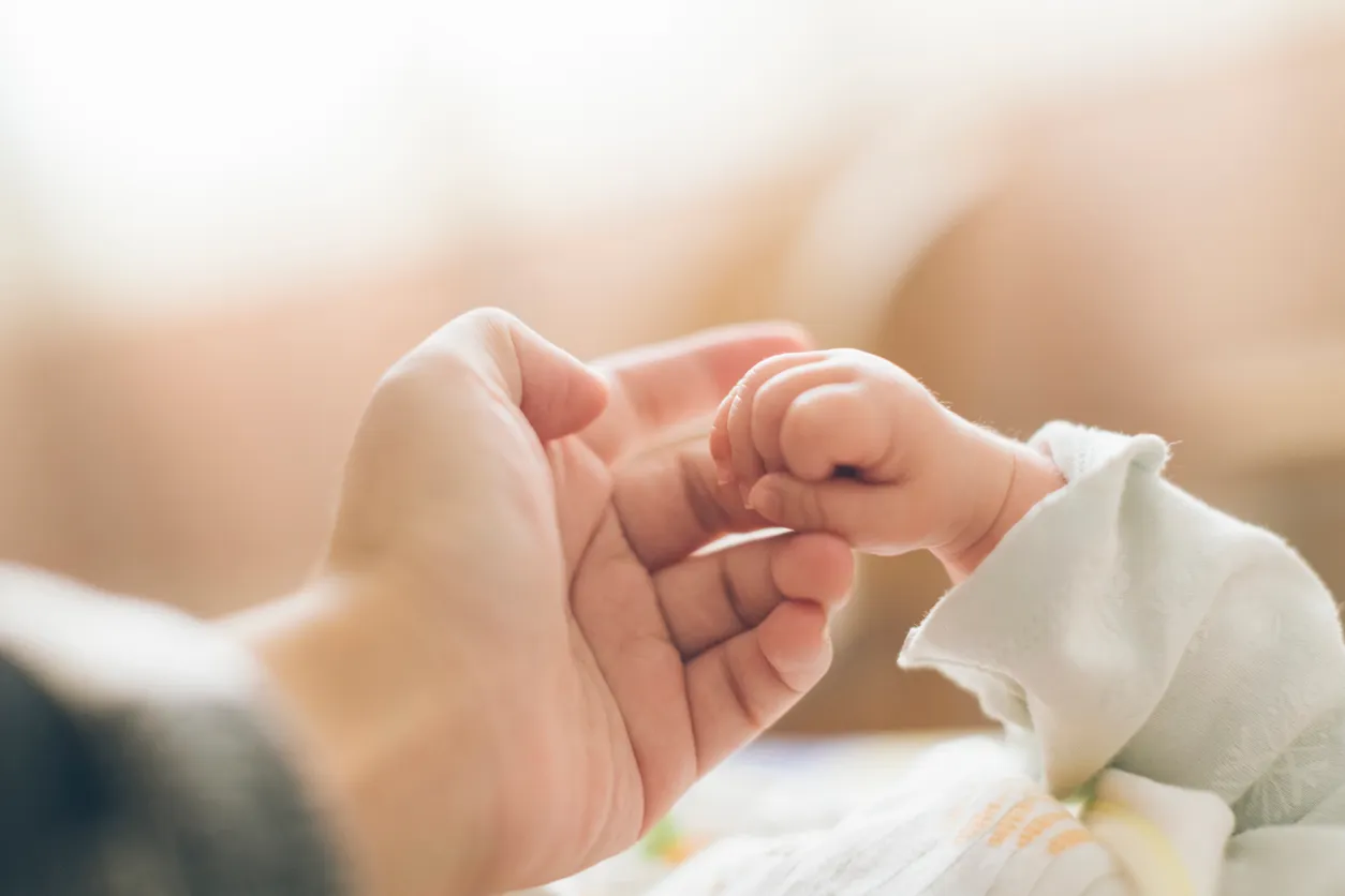 A newborn baby's tiny hand gently gripping a parent's finger in soft light, capturing the tender bond that postpartum depression therapy helps protect.