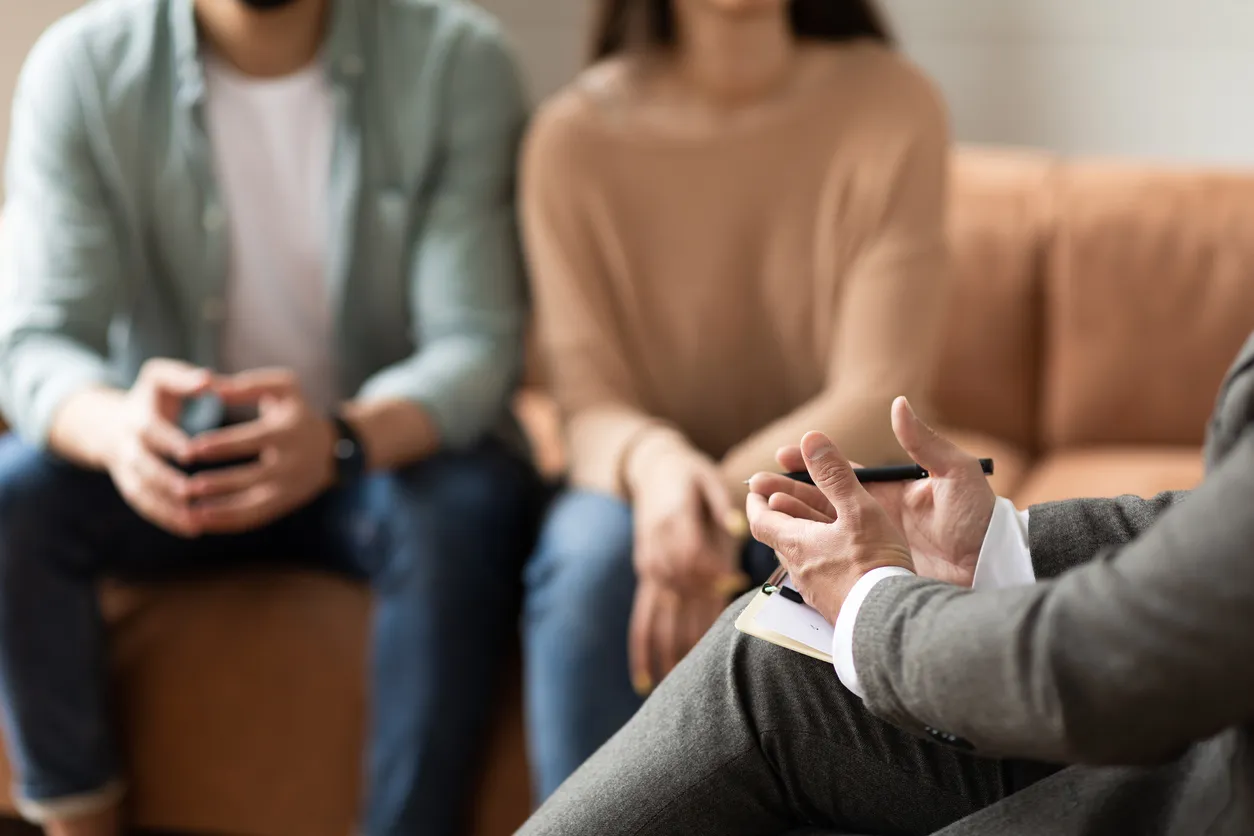 A counselor gestures while speaking with a couple seated on a couch during a divorce and separation counseling session.
