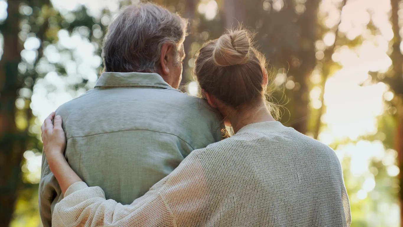 An older father and adult daughter embracing while looking out at sunlit trees, reflecting the restored closeness that family conflict counseling can bring.