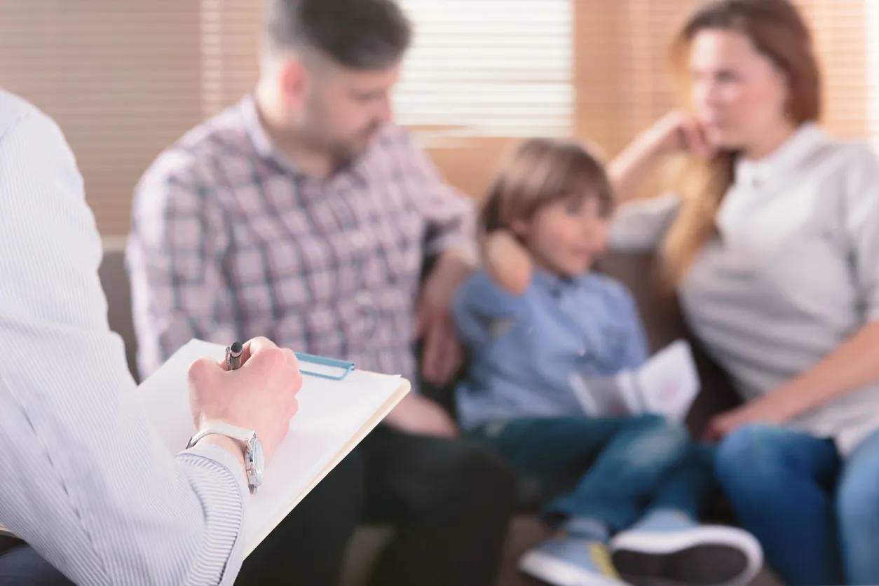A counselor takes notes while a mother, father, and young child sit together on a couch during a parenting counseling session.