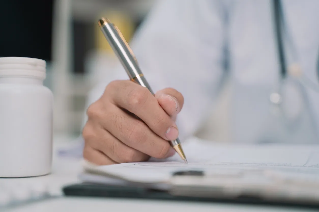 A doctor writes a prescription at a desk with a medication bottle nearby, representing the careful, personalized approach of medication management.
