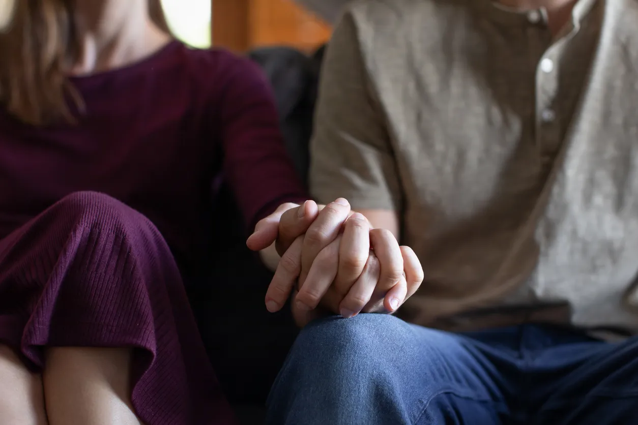 A couple intertwines their fingers while seated together on a couch, a small gesture of unity at the heart of couples counseling.