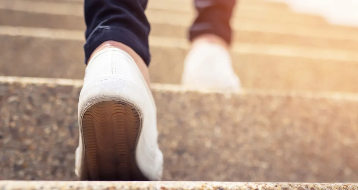 The feet of a person taking steps forward up a staircase, representing taking steps forward in ones life