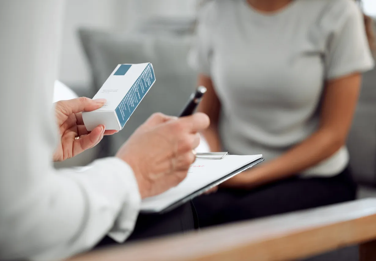 A doctor holds a medication box while reviewing notes with a patient during a depression psychiatry appointment, showing the collaborative approach to treatment.