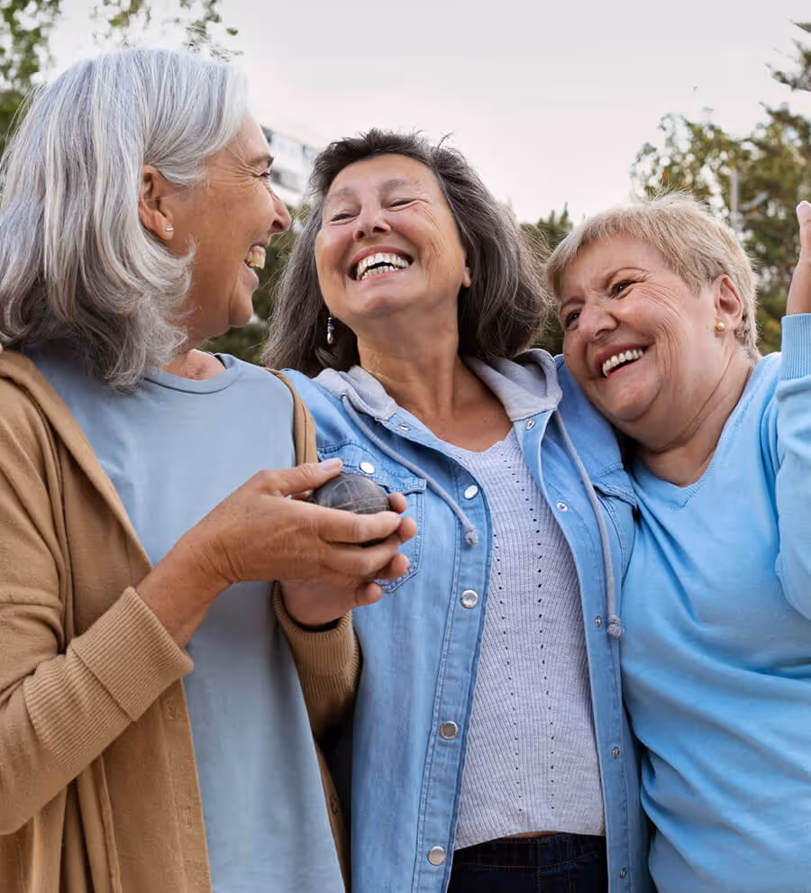 Three older women outdoors smiling and embracing each other joyfully.