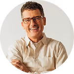 Smiling middle-aged man with glasses wearing a beige button-up shirt against a plain background.