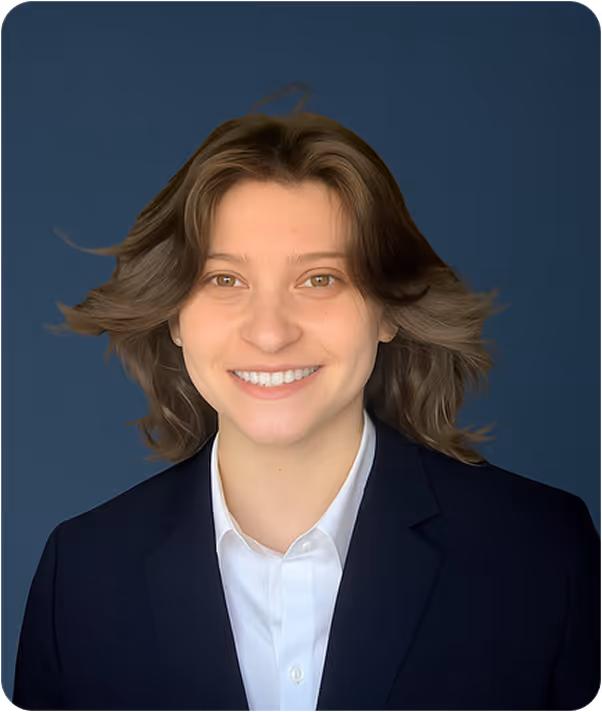 Smiling young person with shoulder-length brown hair wearing a white shirt and dark blazer against a solid dark blue background.