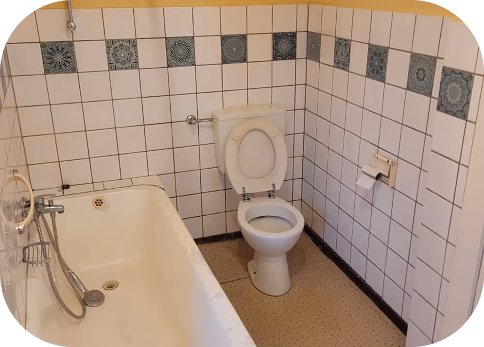 Badezimmer mit Badewanne, offenem WC-Sitz und weißen Wandfliesen mit blauen Mustern.
