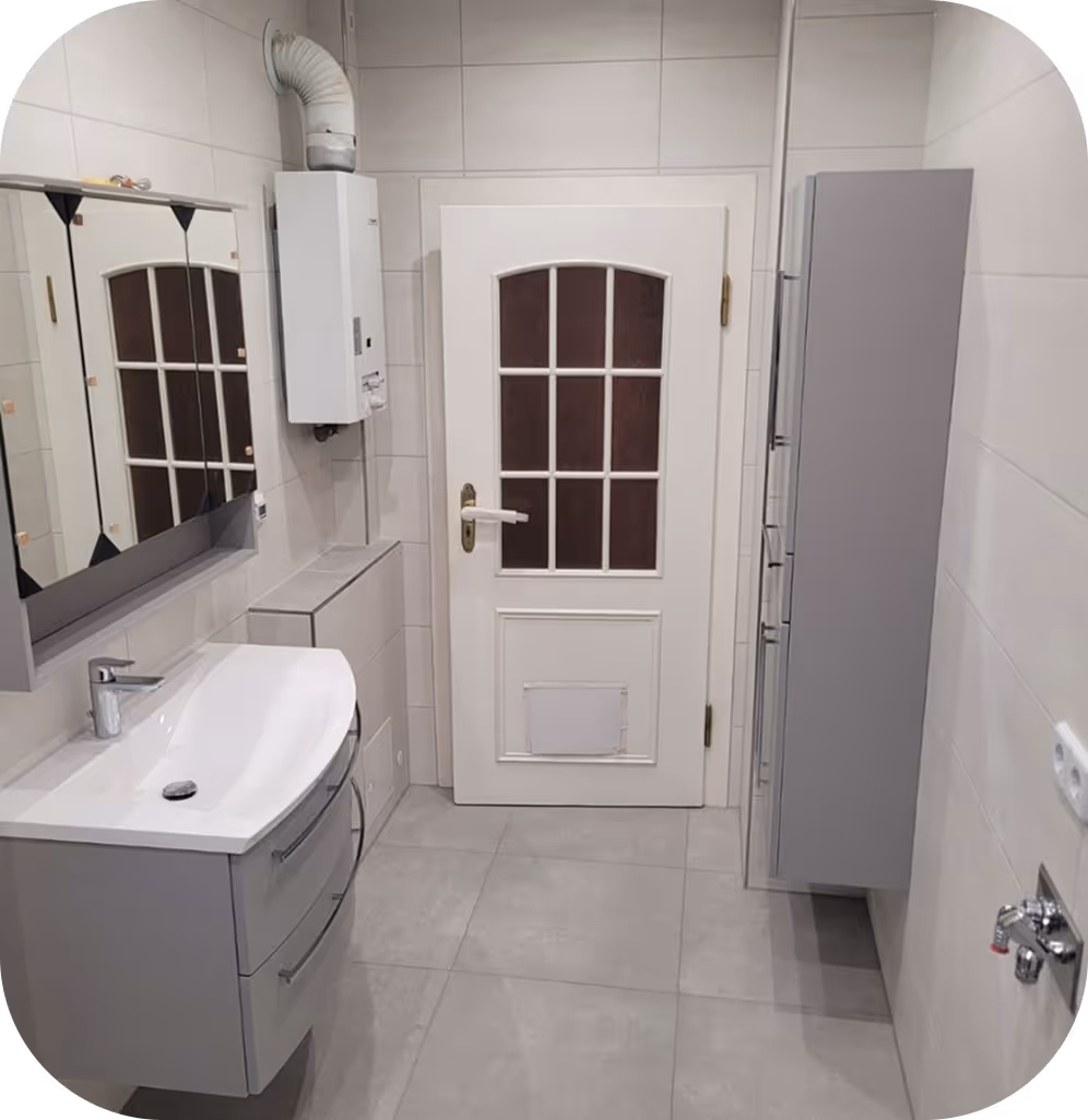 Moderner weißer Badezimmerwaschtisch mit Spiegel, Heizgerät an der Wand und grauer Schrank neben einer weißen Tür mit Glasfenstern.