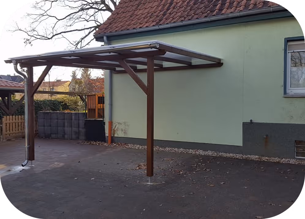 Holzüberdachung mit transparentem Dach an der Seite eines Hauses mit grünem Außenputz.