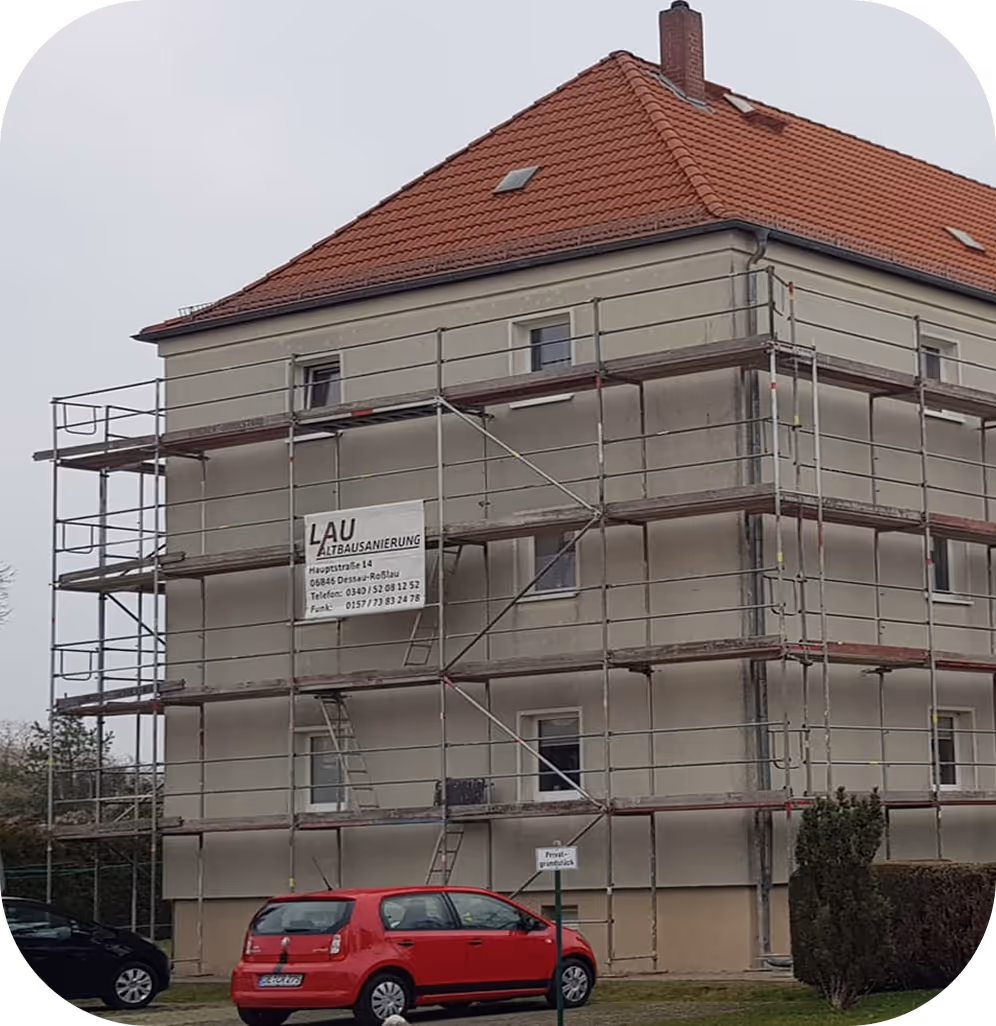 Ein Mehrfamilienhaus mit Baugerüst und einem roten Auto im Vordergrund.