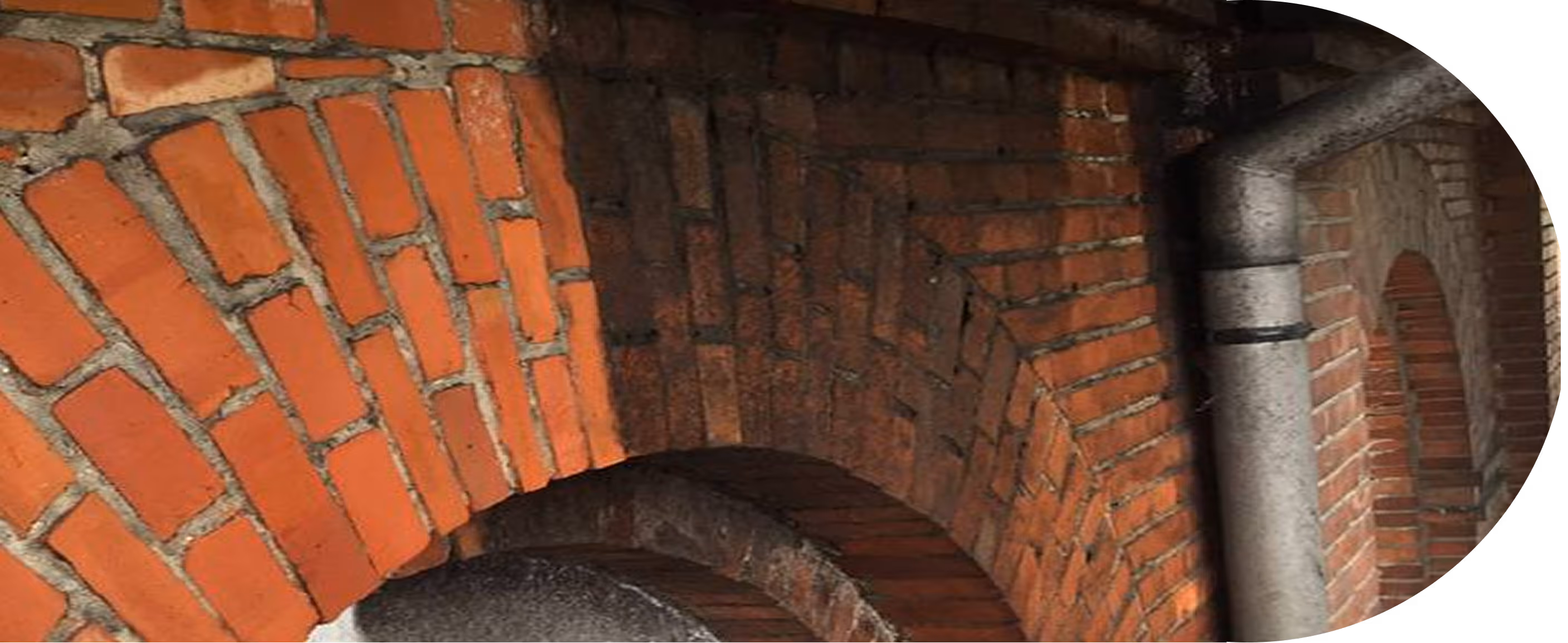 Detailaufnahme eines roten Backsteinbogens mit einem grauen Fallrohr an einer Wand.