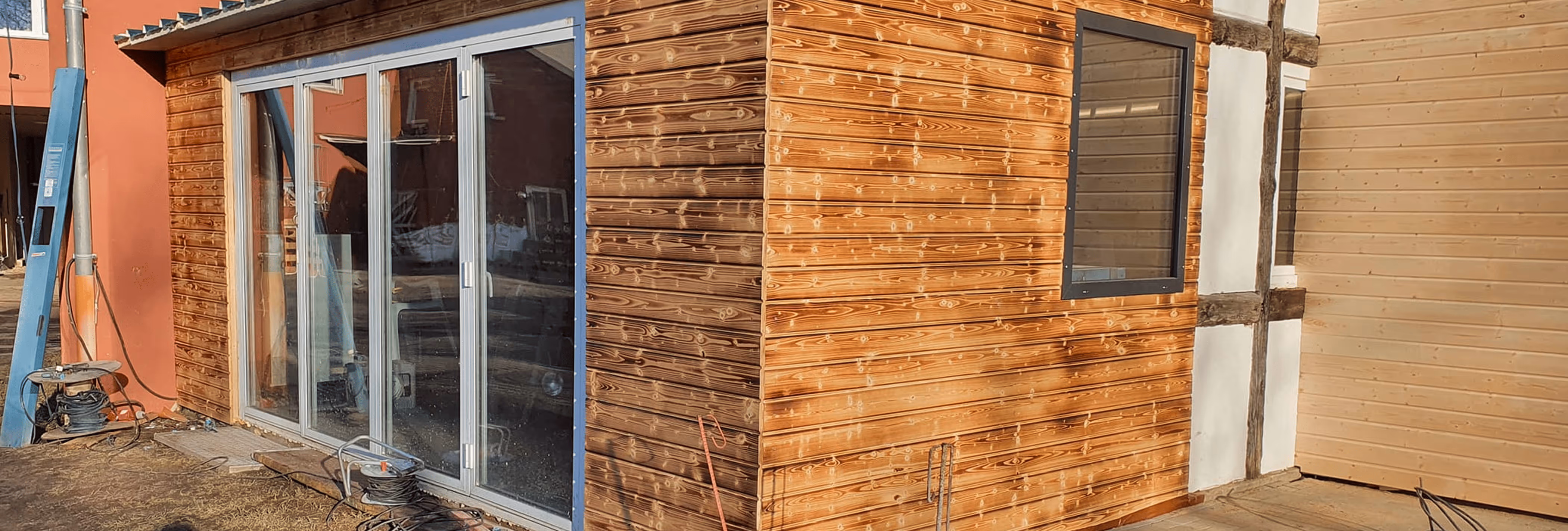 Holzhaus mit großen Glas-Schiebetüren, kleinem Fenster und angrenzendem Gebäude mit Fachwerk.