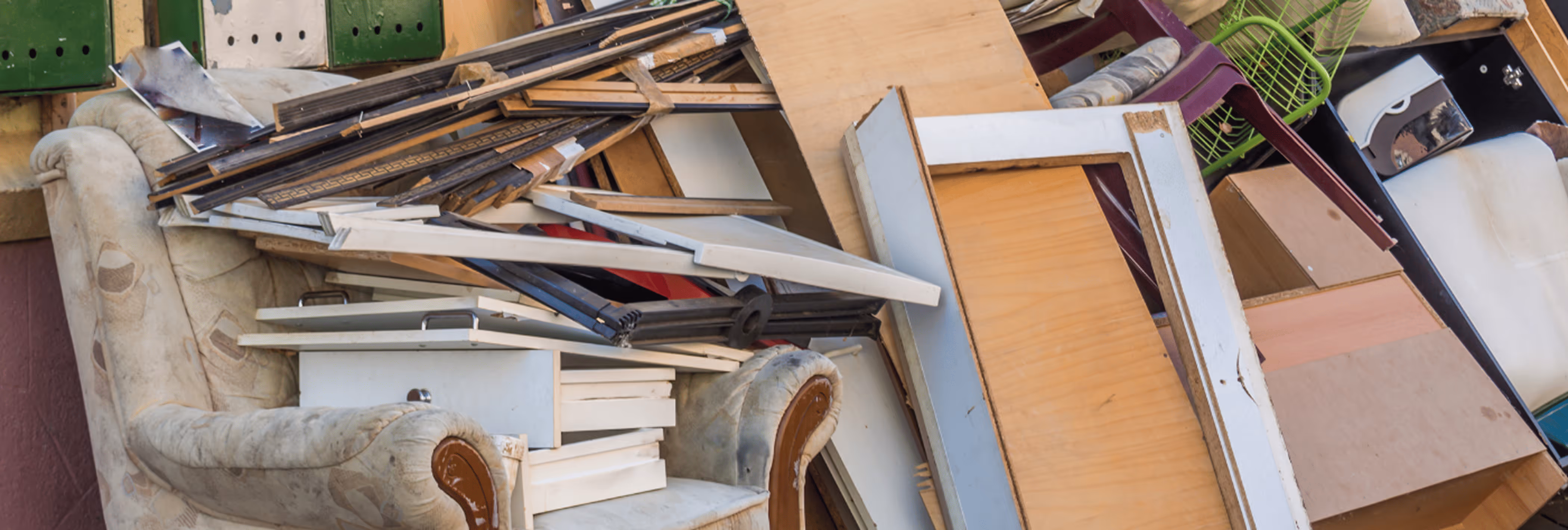 Alte Möbel und Holzplatten, die auf einem Sofa gestapelt sind, in einem Haufen entsorgter Haushaltsgegenstände.