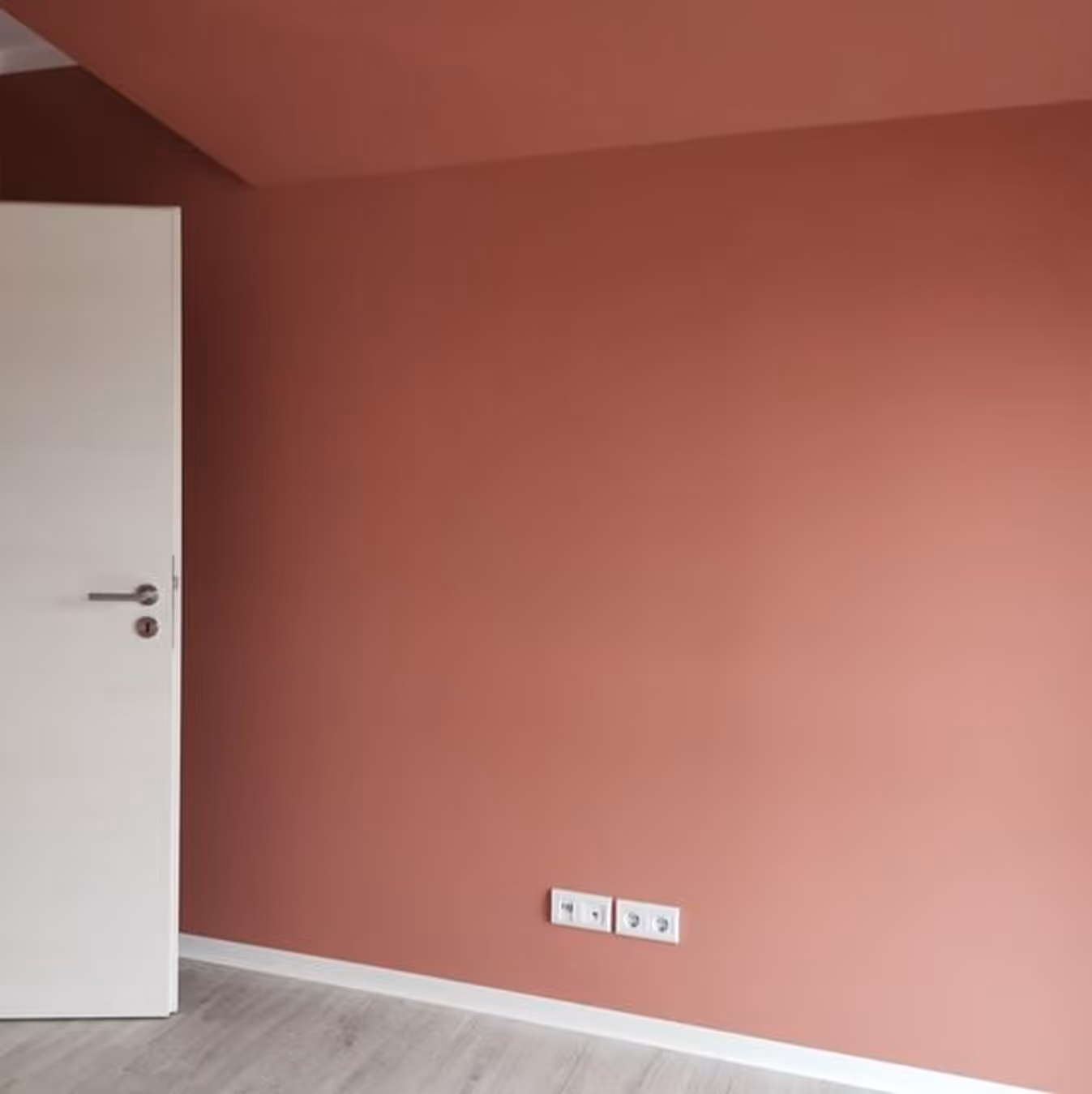 Leere Wand in einem Raum hellbraun gestrichen mit einem weißen Türblatt links und Holzboden.