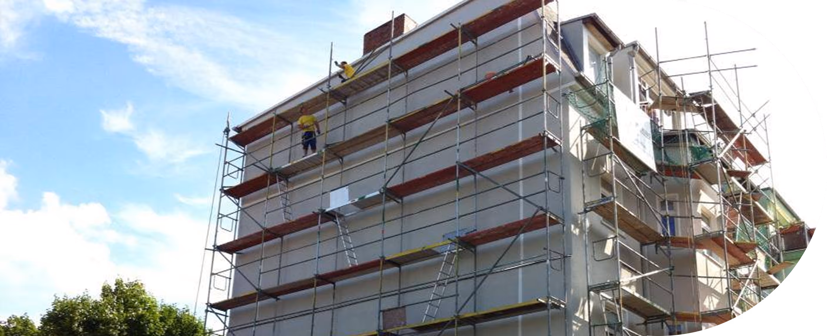 Gebäude unter Renovierung mit Gerüst und zwei Bauarbeitern an der Fassade bei klarem Himmel.