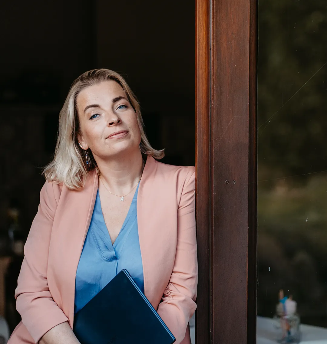 Anne Hütter lächelt einladend an einer Tür lehrend mit einem Tablet im Arm – Kontaktmöglichkeit für Austausch, Termine und Coaching-Anfragen bei annesstar.com in Lüneburg.