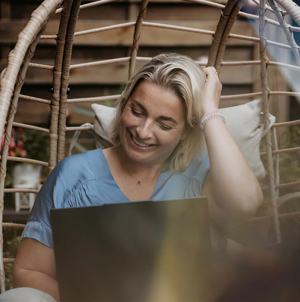 Anne Hütter sitzt entspannt und lächelnd mit einem Laptop im Hängesessel im Freien (Natur-Setting) – Symbol für Naturverbundenheit, intuitive Weisheit und spirituelle Werte als wesentlicher Teil ihres hybriden Coaching-Ansatzes bei annesstar.com für den D-A-CH-Markt.