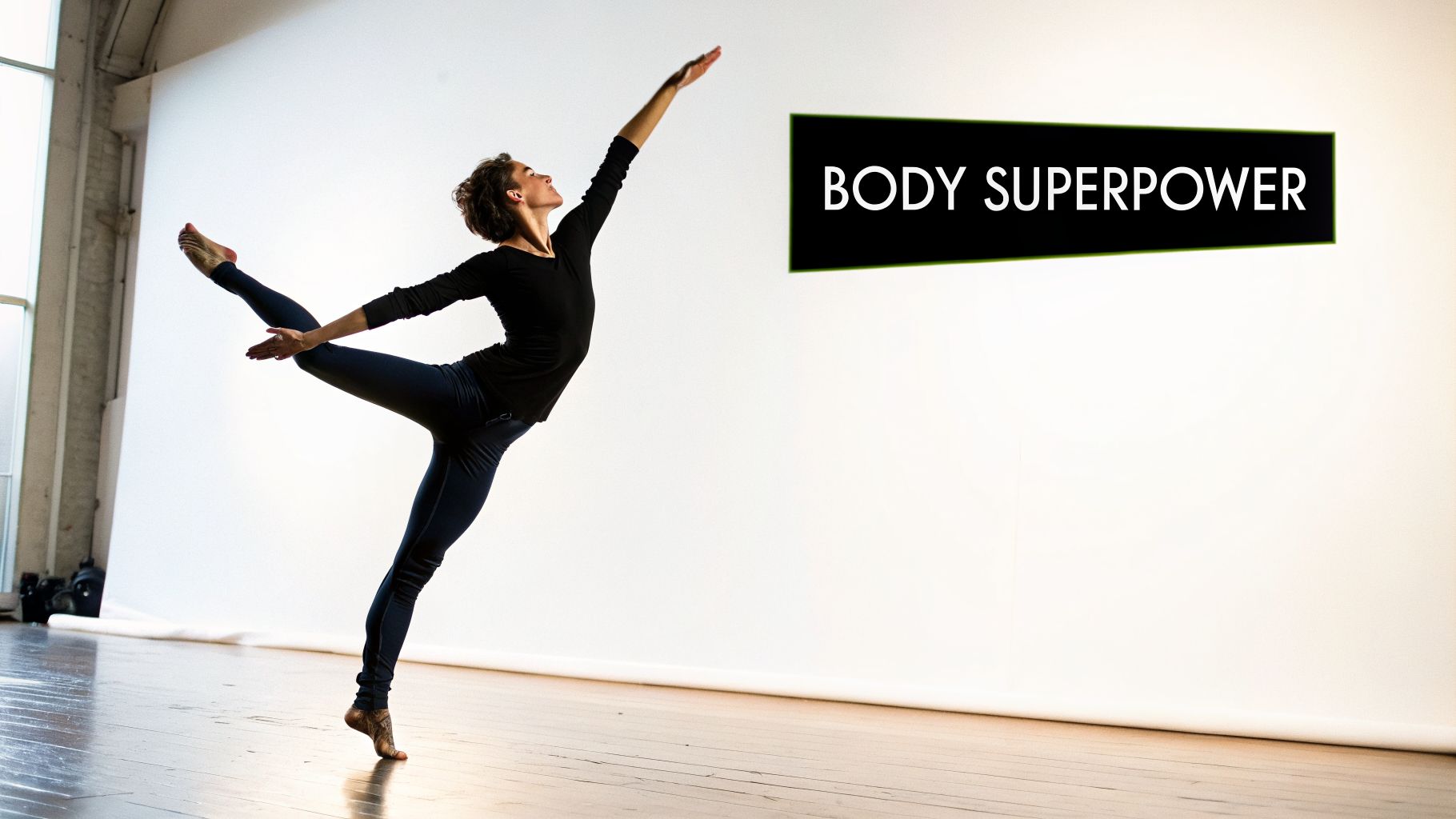 A female dancer in dark attire performs a graceful pose, balancing on one leg, against a white background.