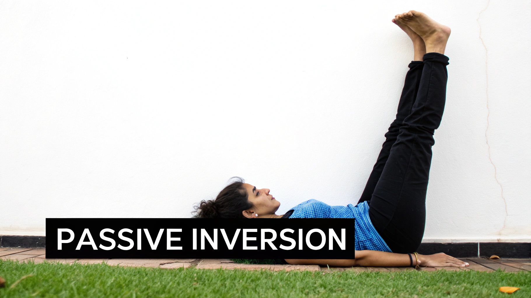 A person lies on their back, performing a passive inversion yoga pose with legs against a white wall.