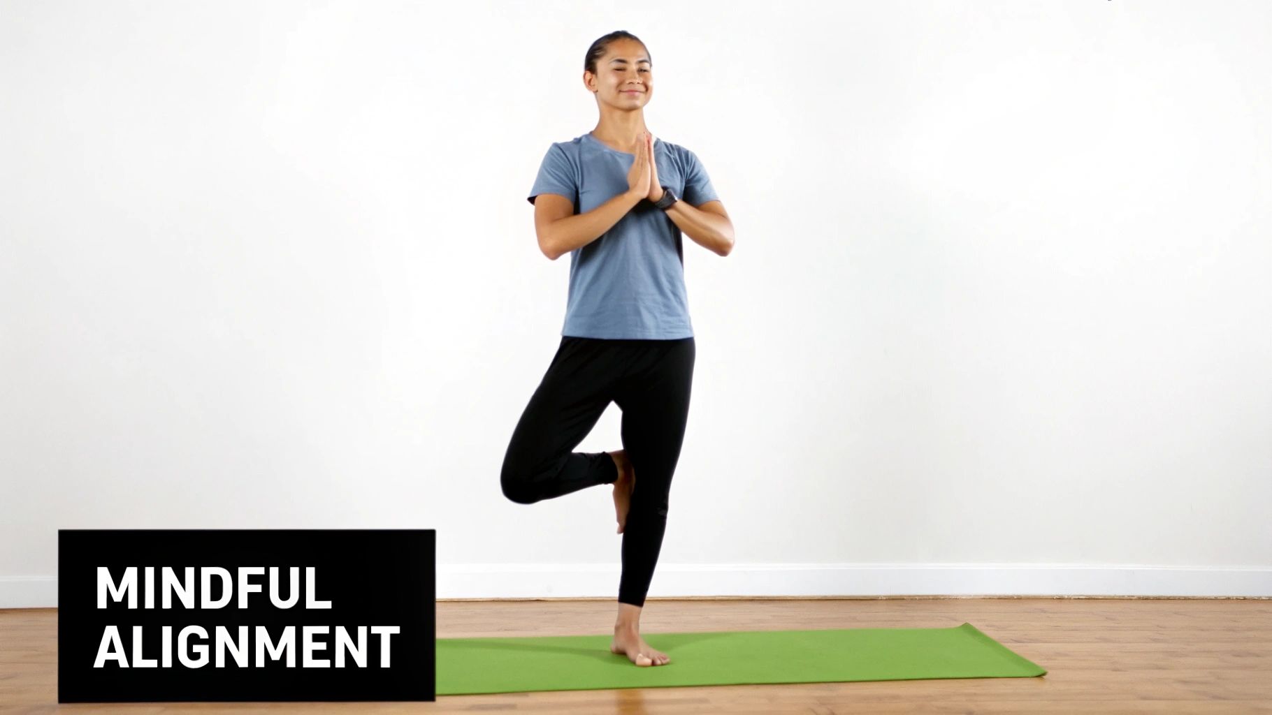 Smiling woman in Tree Pose on a green yoga mat, demonstrating mindful alignment.