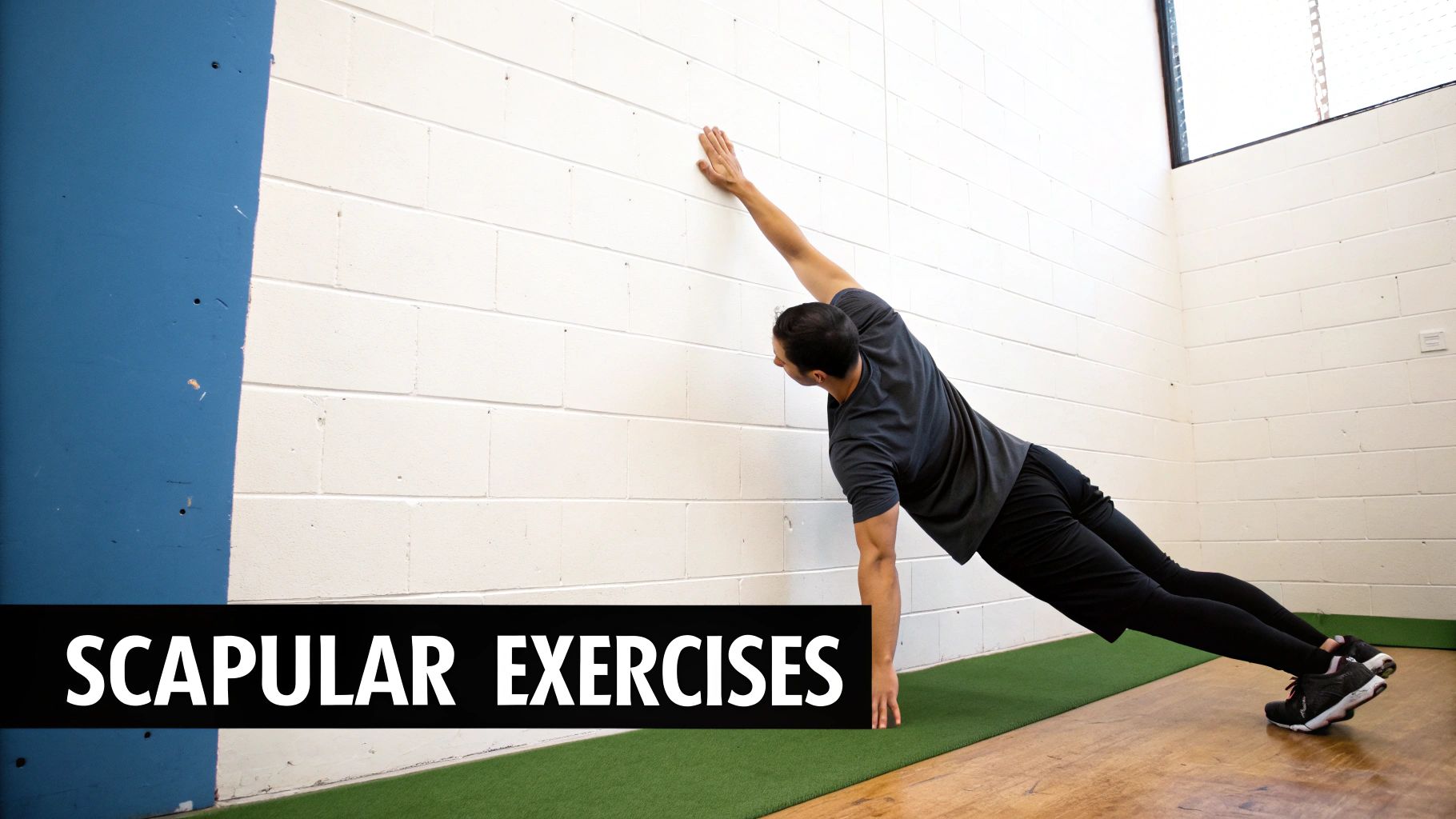 A man performs a scapular exercise, leaning against a white brick wall with one arm extended.
