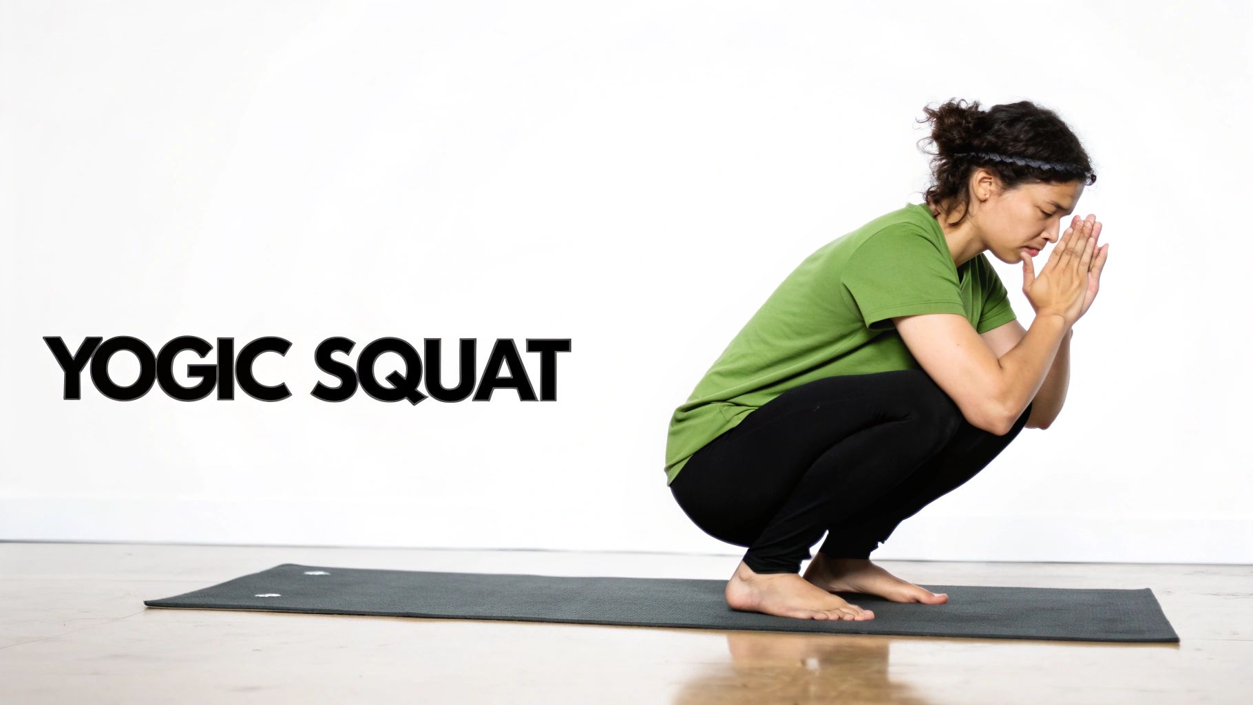 A person in a yogic squat (Malasana) pose on a dark yoga mat with hands in prayer.