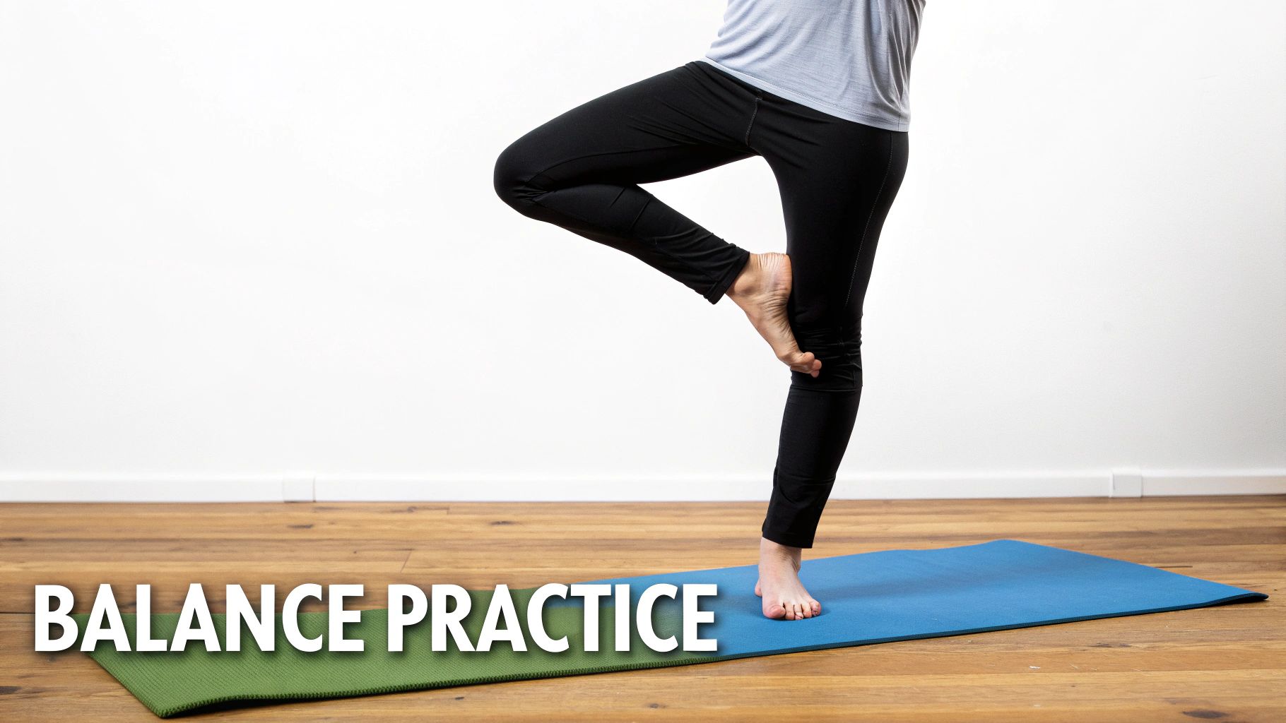 A person in black leggings and a grey shirt performing a tree yoga balance pose on a blue mat.