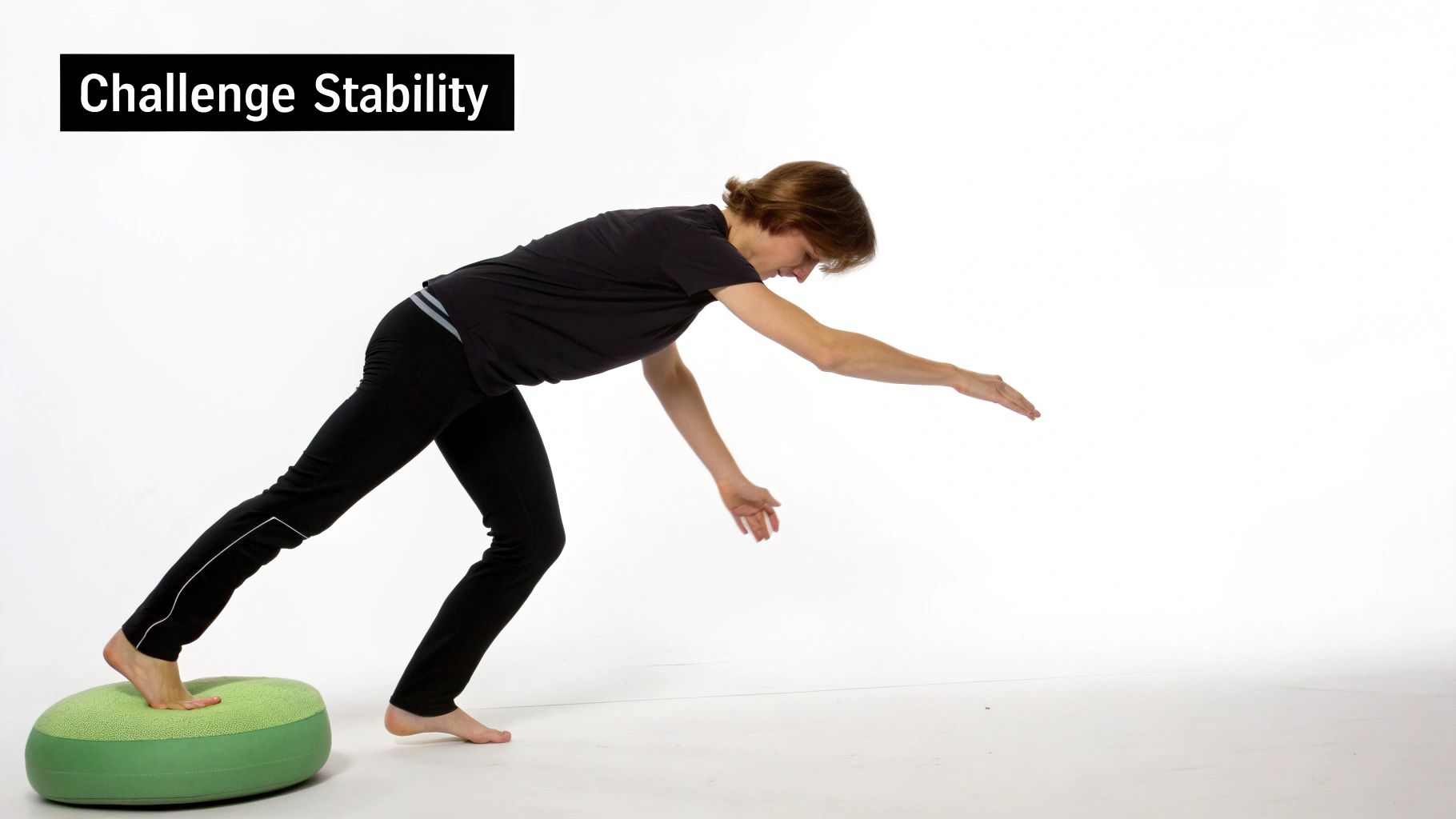 A person balances on a green stability cushion, leaning forward with arms extended to challenge balance.