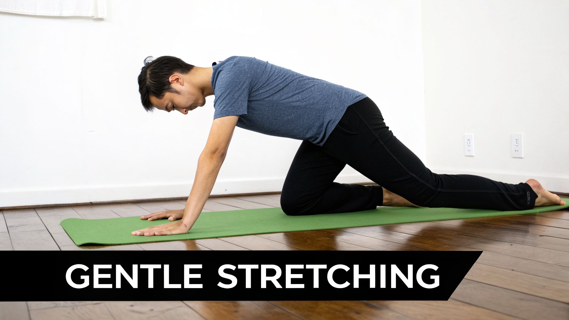 A man in a blue shirt stretching on a green yoga mat, in a gentle quadruped position.