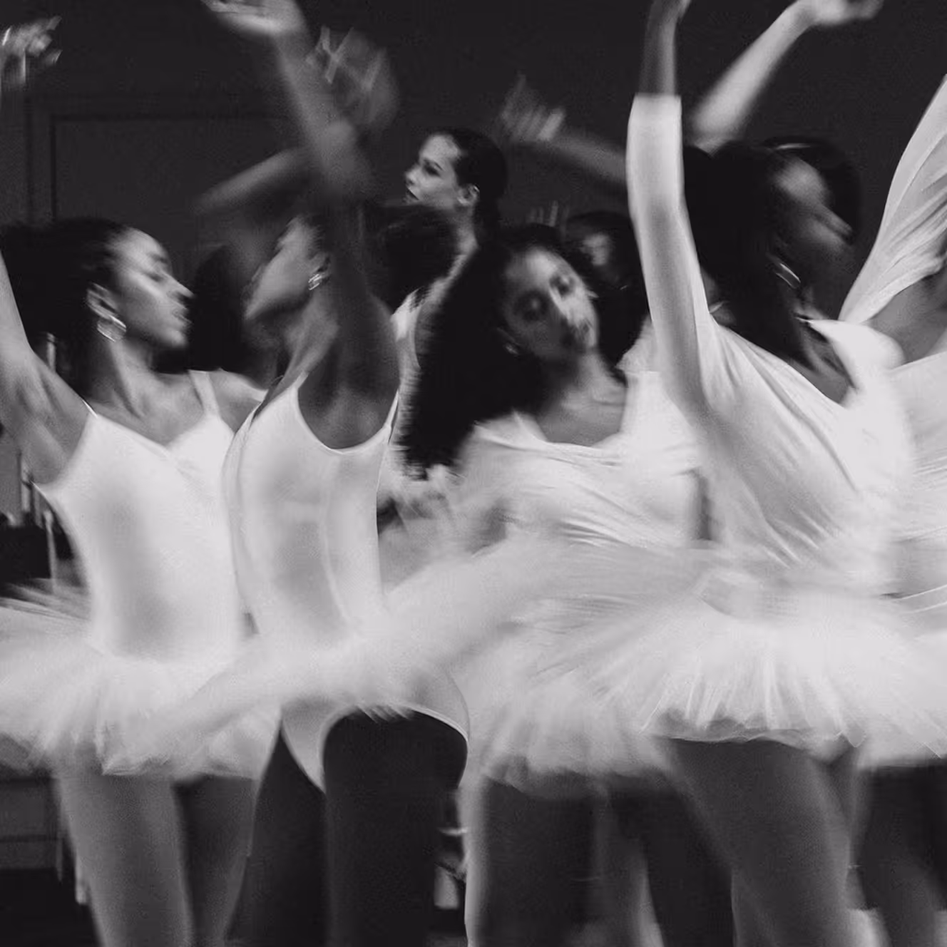 Black and white photo of multiple ballerinas in white tutus spinning with blurred motion.