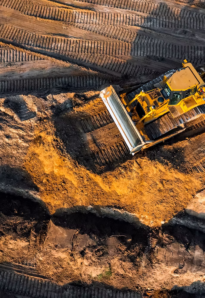 Aerial view of a yellow bulldozer moving soil on a construction site with visible tire and track marks.