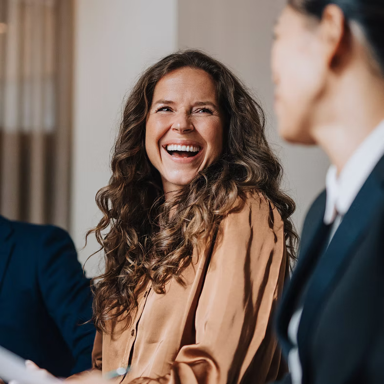 A woman with long curly hair laughing and looking at another person in a business setting.