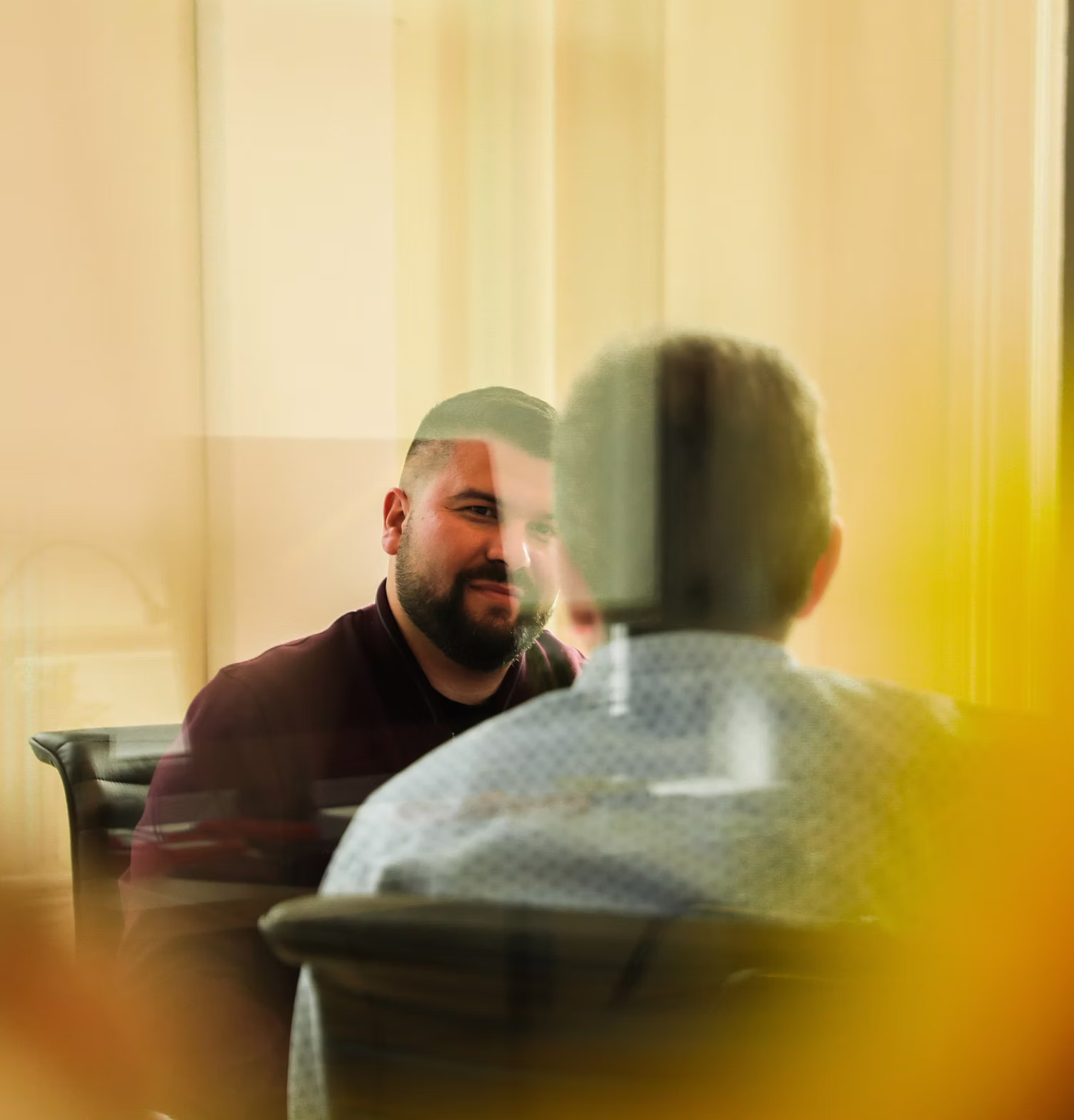 Two men having a conversation across from each other in an office setting, viewed through a glass partition.