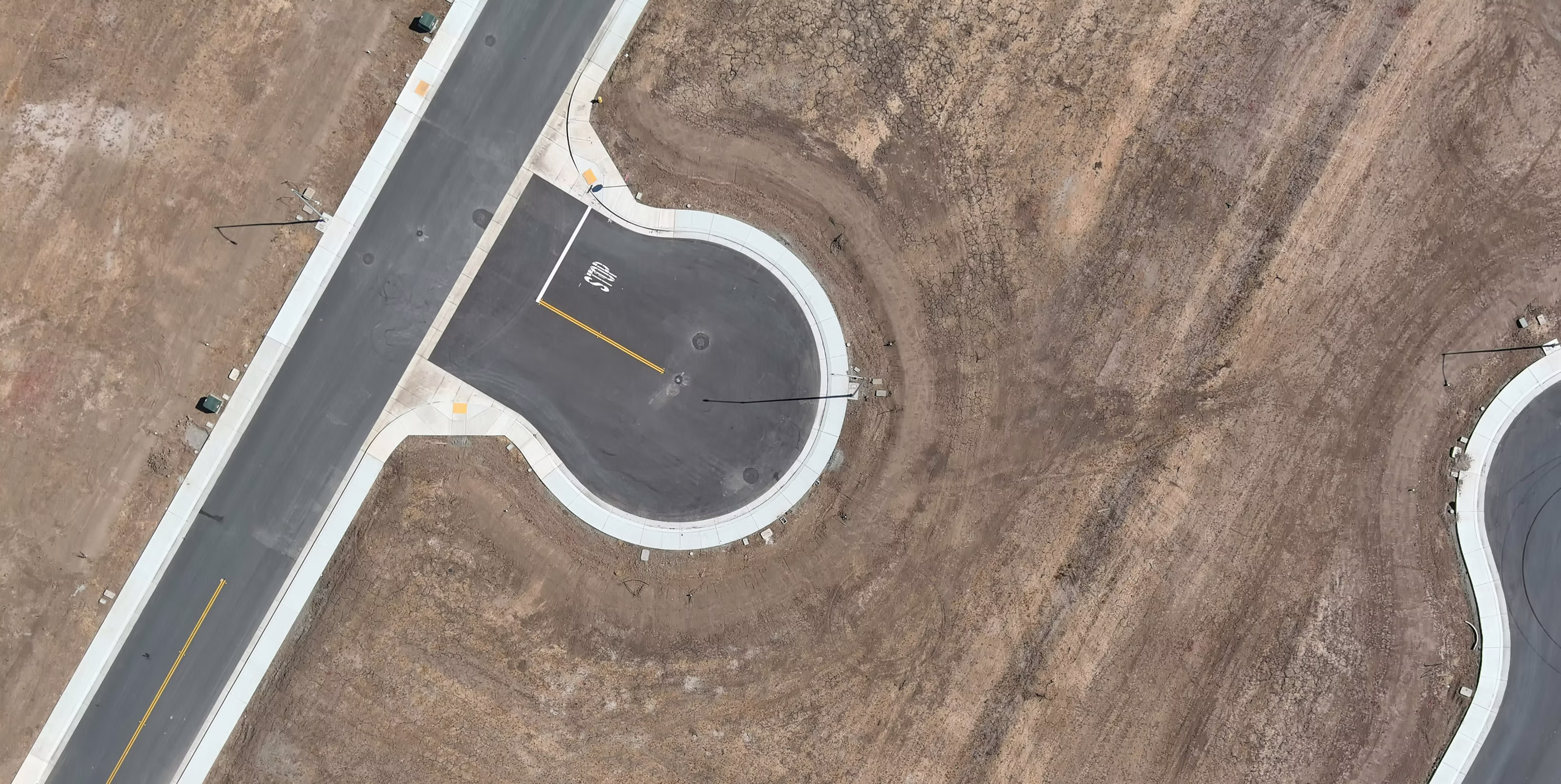 High-angle aerial view of a newly paved asphalt cul-de-sac and residential street, showing clean infrastructure and ready-to-build land plots.