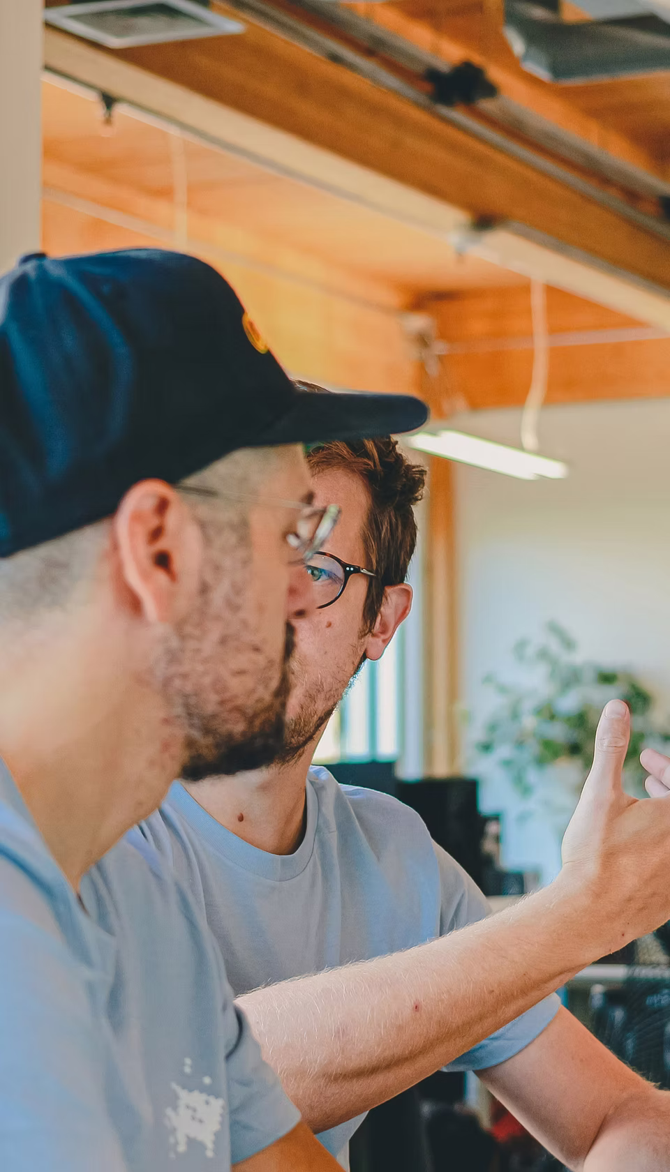 Close-up, candid shot of two real estate professionals in a light-filled, wood-beamed office engaging in a collaborative discussion.