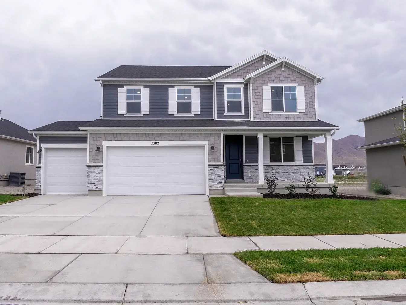 Modern two-story house with gray siding, white garage doors, and a small front porch with a blue front door.