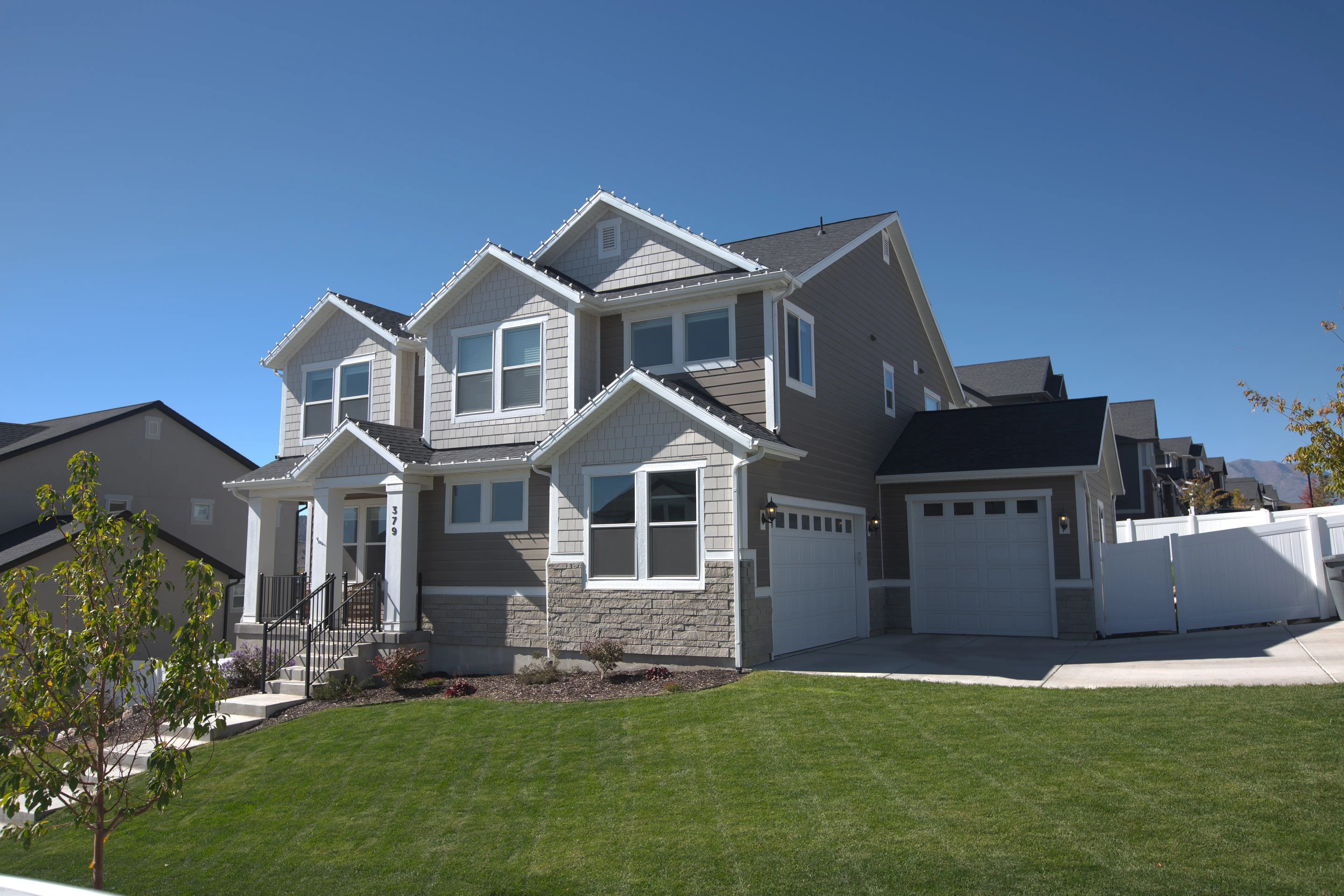 Modern two-story suburban house with gray siding, white trim, two garages, and a well-maintained green lawn.