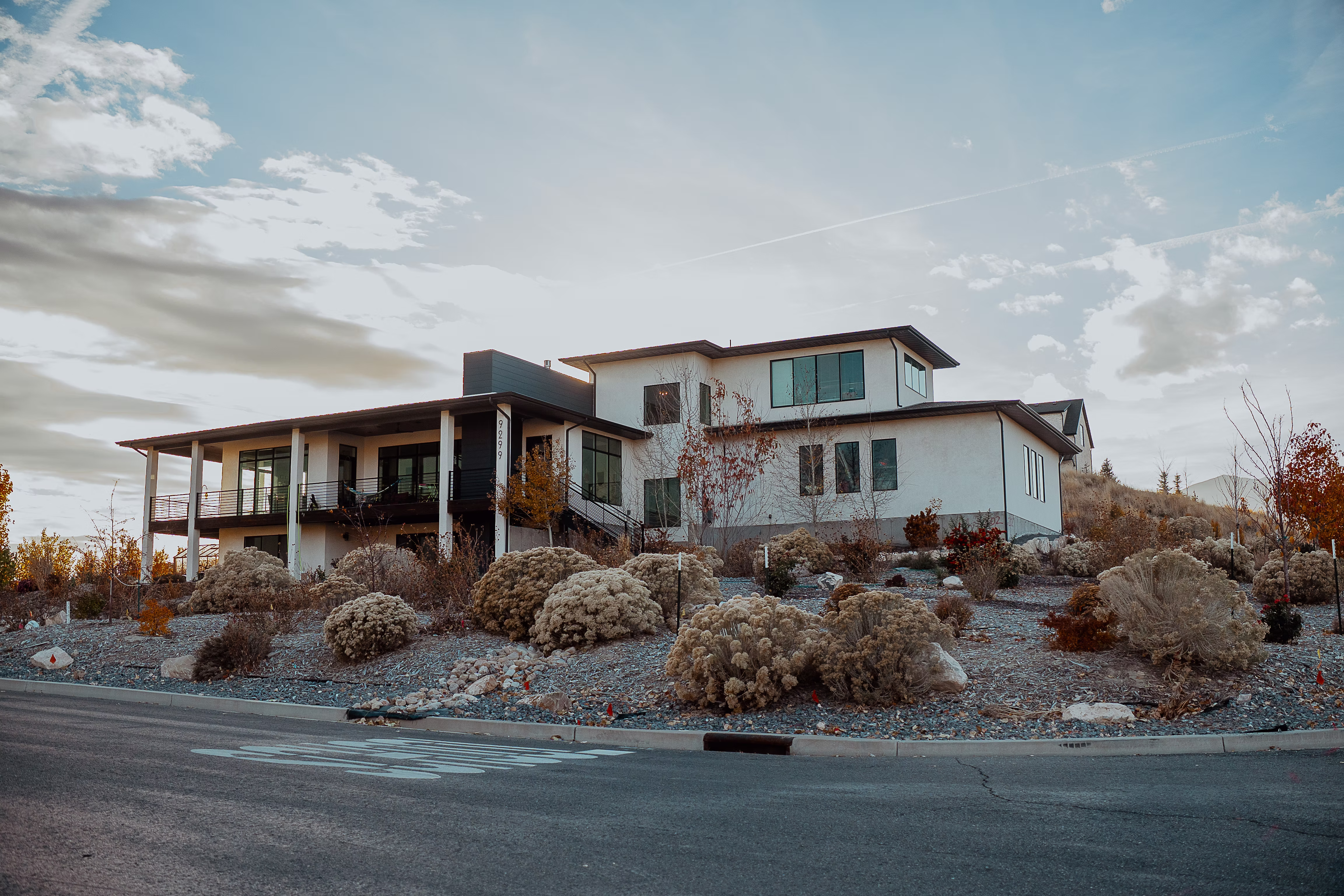 A luxury hillside residence featuring white exterior walls and black window frames, surrounded by meticulously designed drought-tolerant landscaping and shrubs.