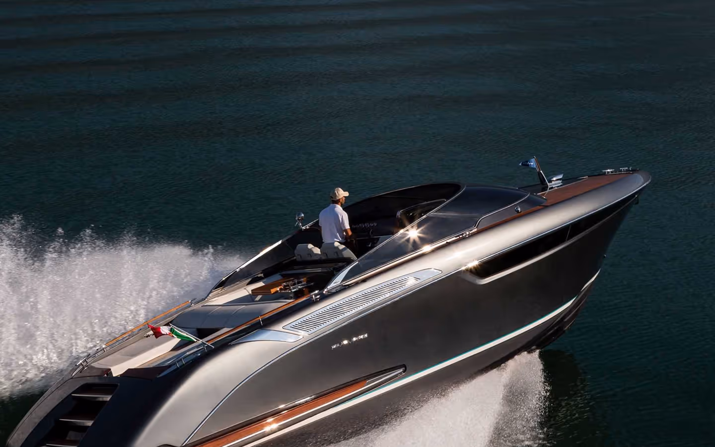 Sleek silver motorboat cruising on calm waters with a person steering at the helm.