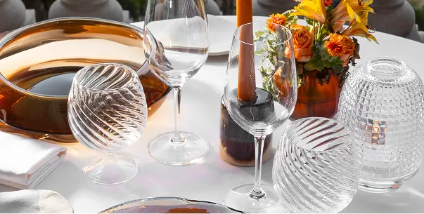 Table set with amber and clear glassware, a candle, flowers in an amber vase, and white napkins on a white tablecloth.