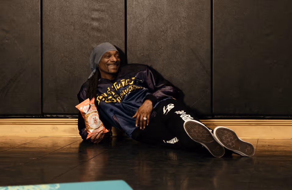 Snoop Dogg holding a bag of Outstanding Foods PigOut pigless pork rinds