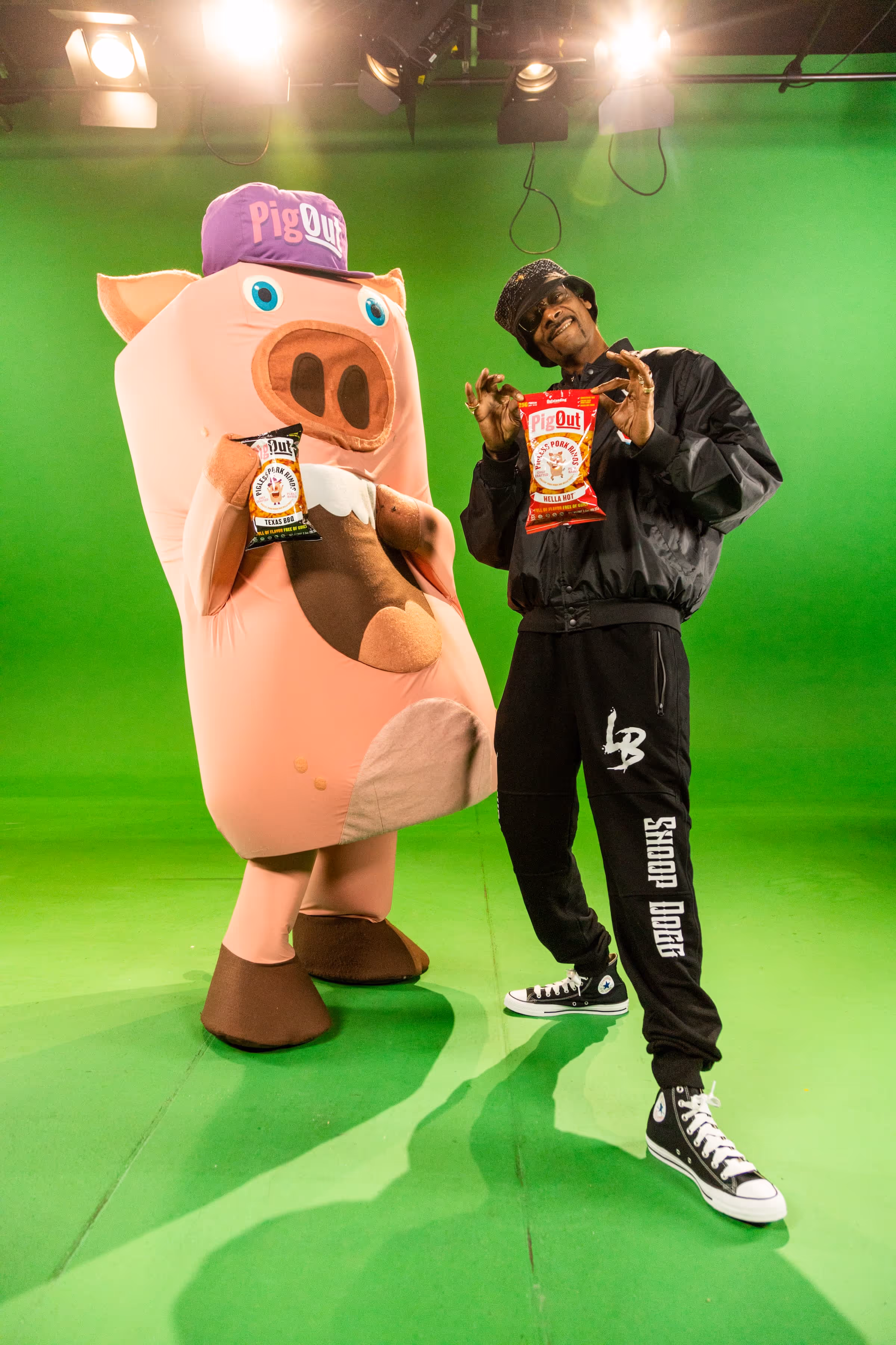 Snoop Dogg posing with Outstanding Foods' inflatable PigOut pig mascot, both holding snack bags