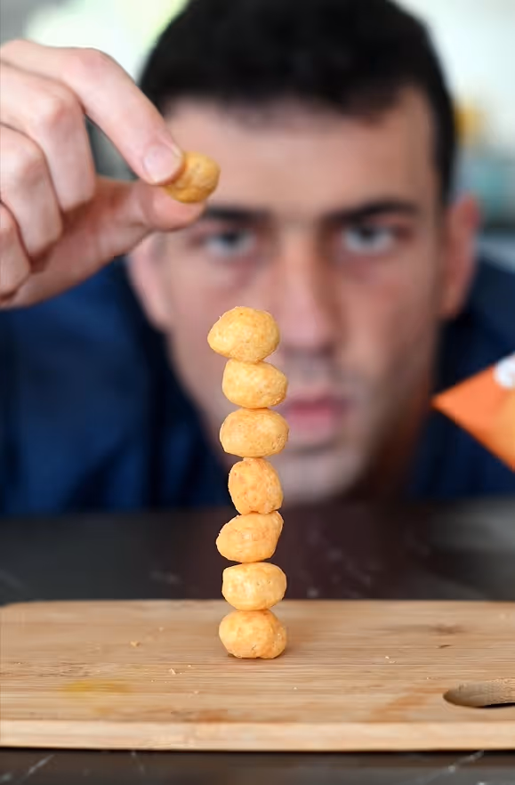 Hand stacking a tower of cheese ball snacks on a wooden board