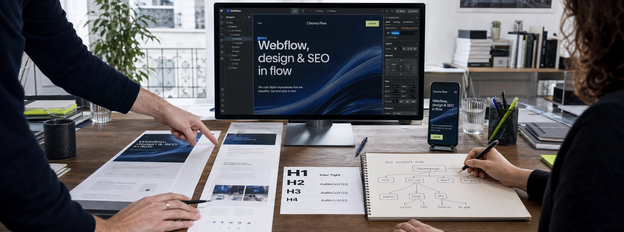 Deux personnes conçoivent un site Webflow Chroma Flow : maquettes imprimées, arborescence SEO manuscrite et le Designer Webflow à l'écran