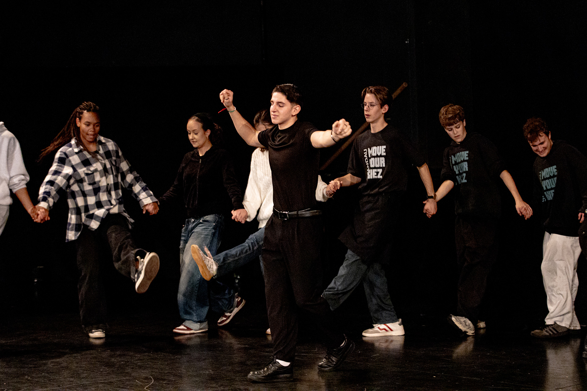 Eine Gruppe Jugendlicher Tanzen auf einer Bühne und halten sich an der Hand