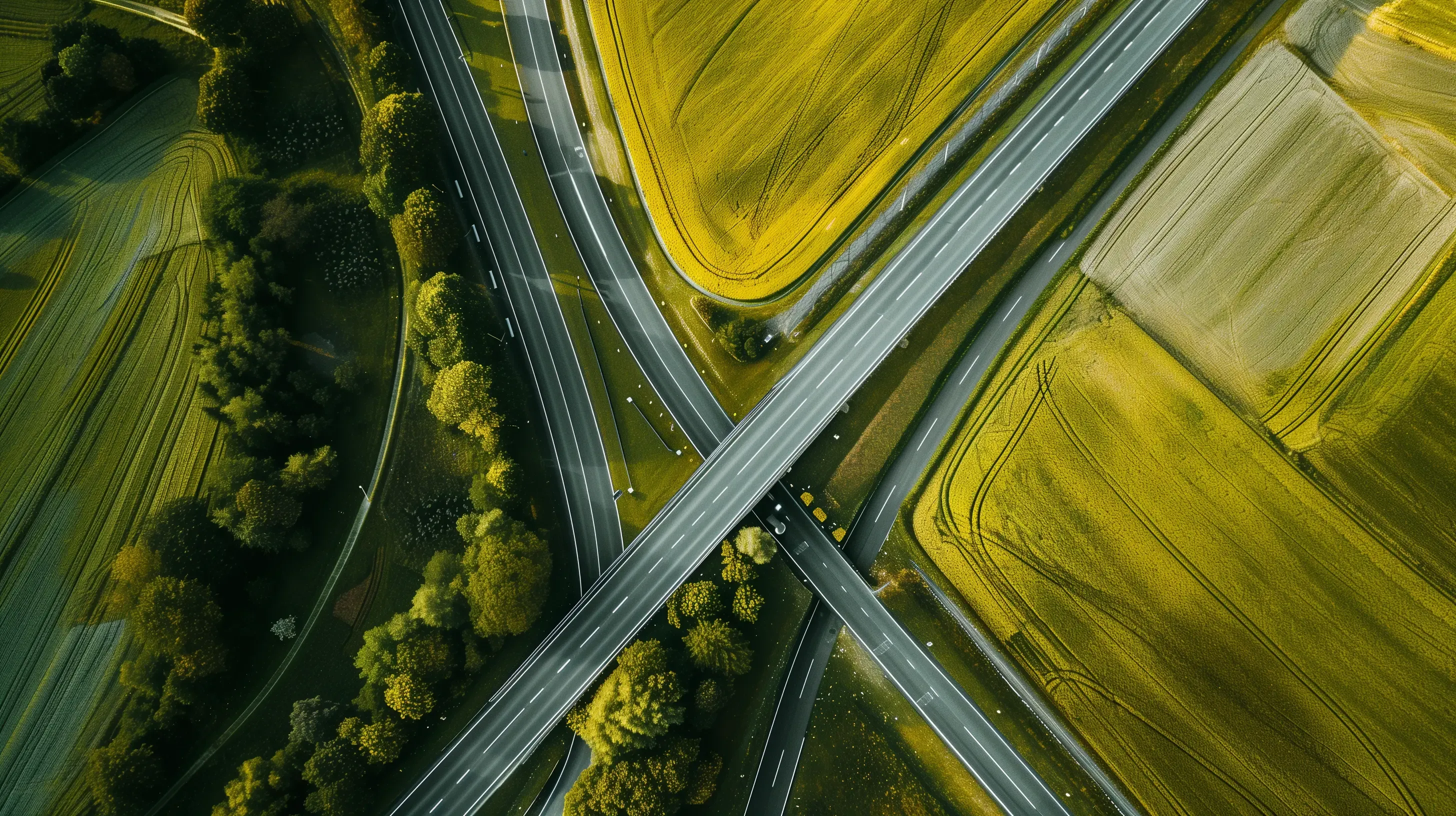 Aerial view of a highway intersection surrounded by green and yellow agricultural fields with trees.