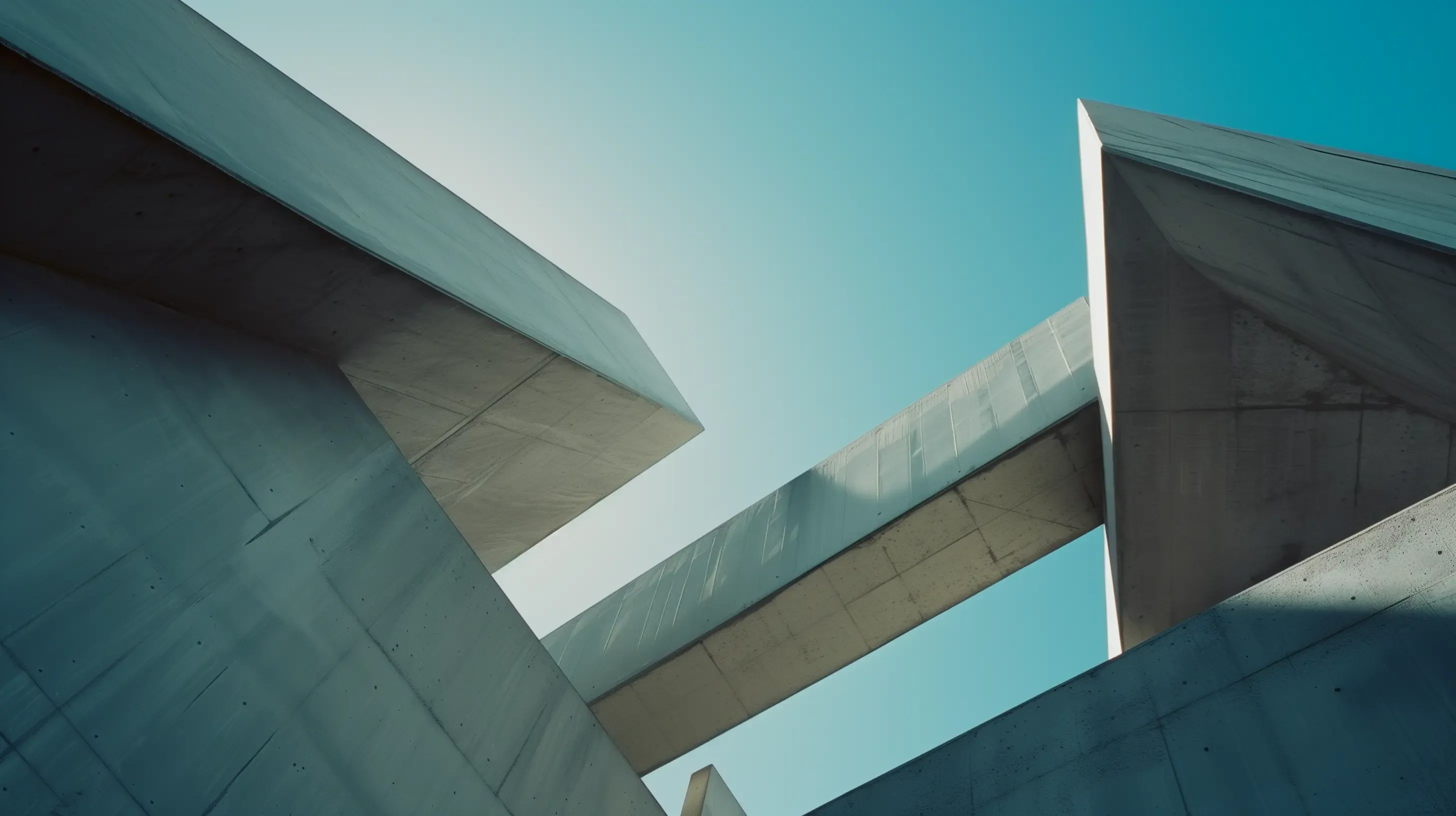 Modern concrete architectural structure with angular forms and a skybridge against a clear blue sky.