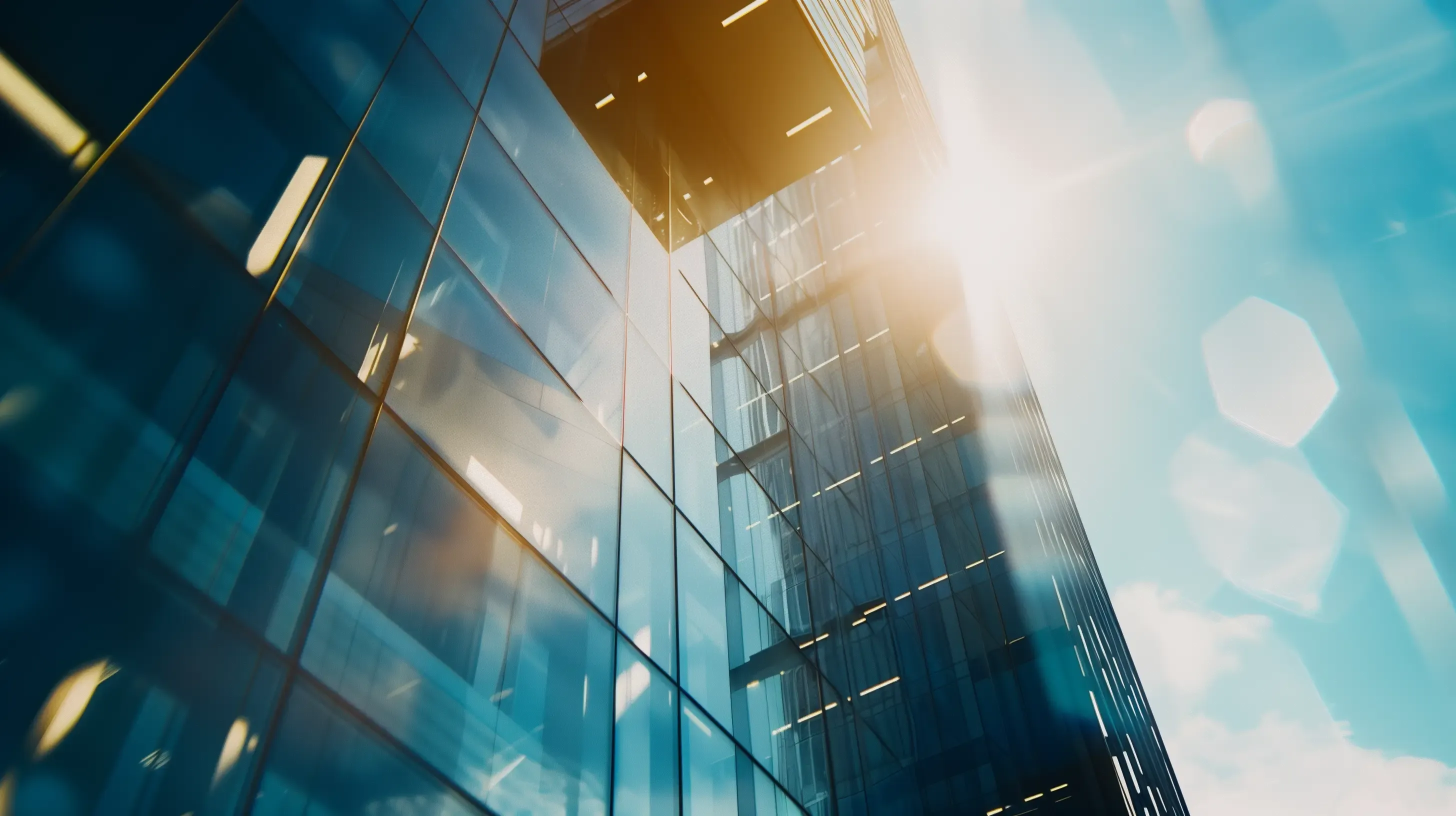 Modern glass building reflecting sunlight with lens flare and blue sky.